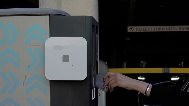 A driver reaching from their car to badge into a parking garage reader